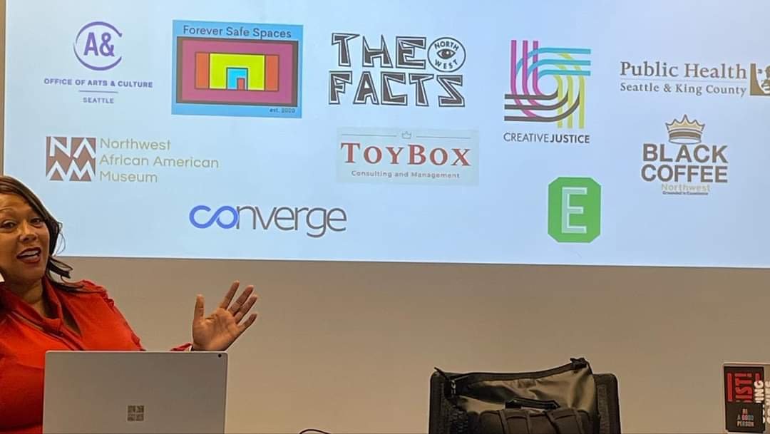 Katoya Palmer presenting at a laptop in front of a screen of partner logos