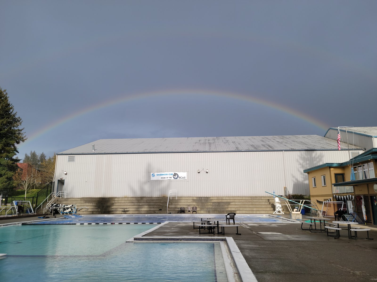A rainbow over a building beside an outdoor swimming pool