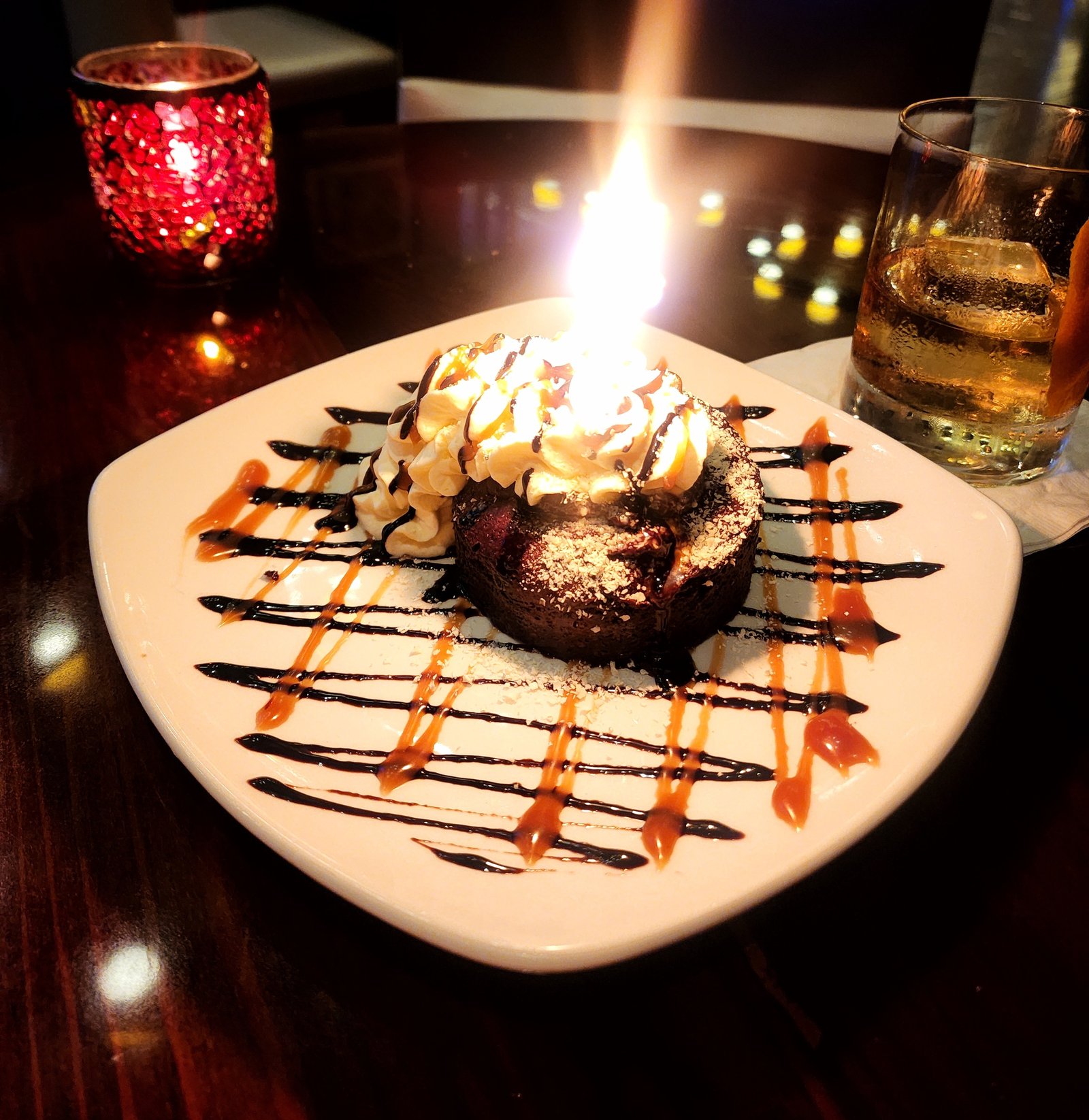 A chocolate dessert with a lit birthday candle on a white plate
