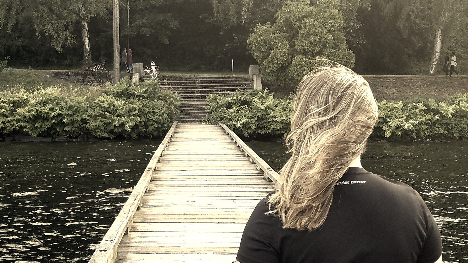 A person seen from behind at the end of a wooden dock over still water