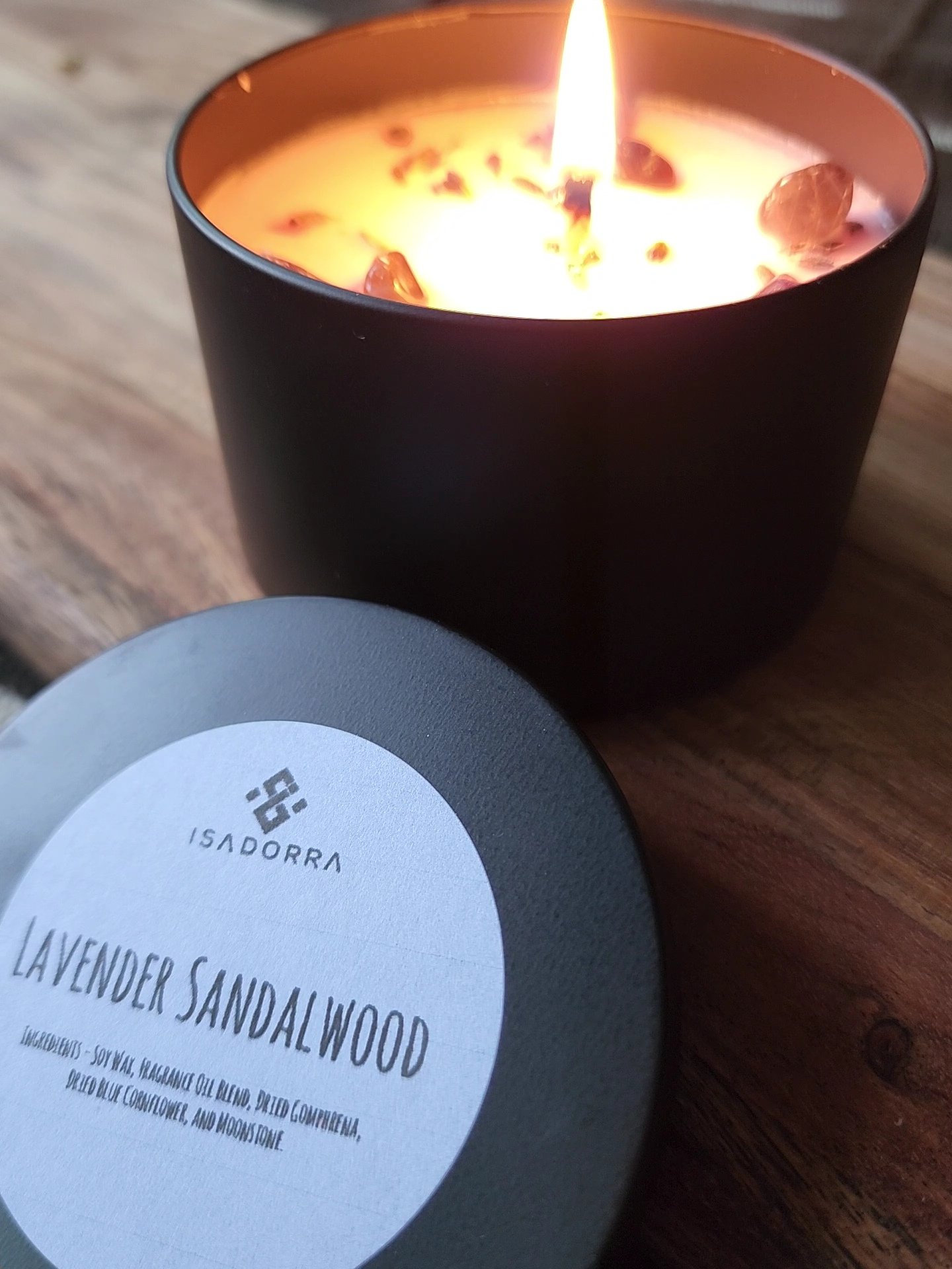 A lit candle beside a Lavender Sandalwood candle tin