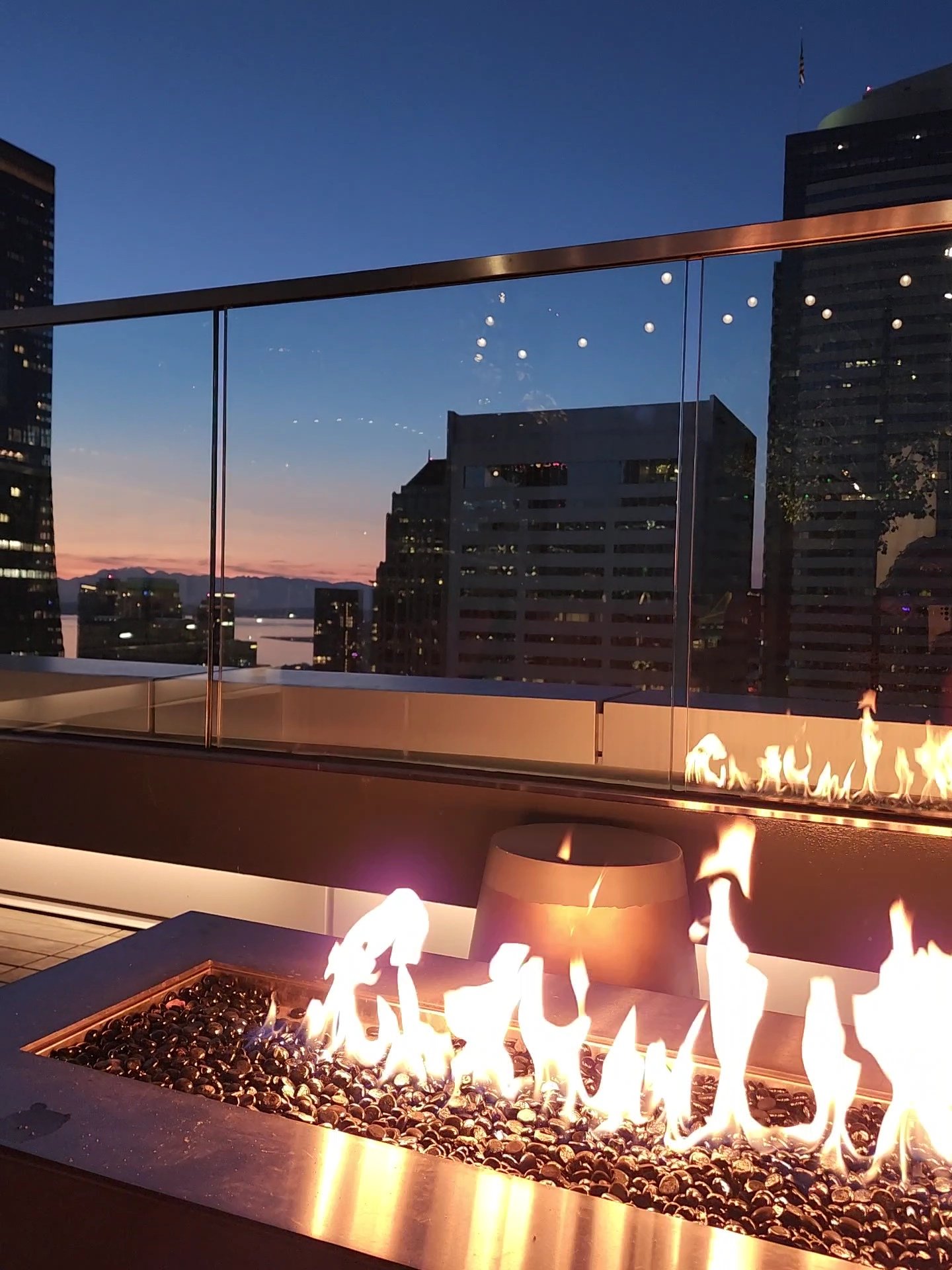 A fire table on a high-rise balcony at dusk, looking out over city towers