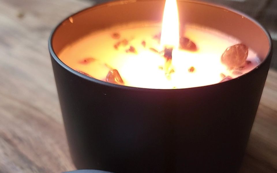 A lit candle in a black tin, glowing on a wooden table